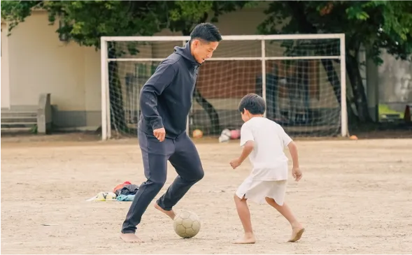 裸足でボールを追う子どもと指導する様子