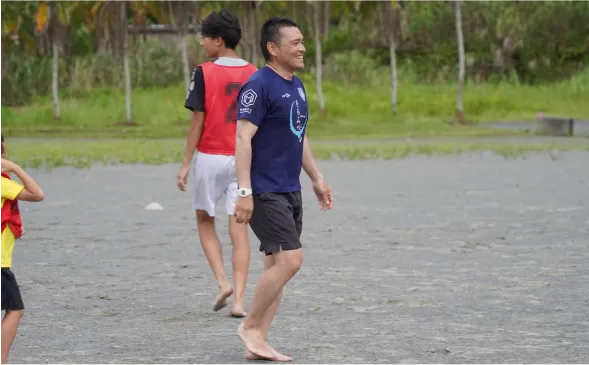 裸足でボールを追う子どもと指導する様子